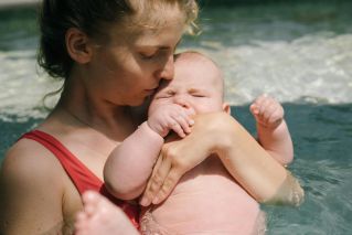 A tender moment of a mother holding her baby in a swimming pool, exemplifying love and care.